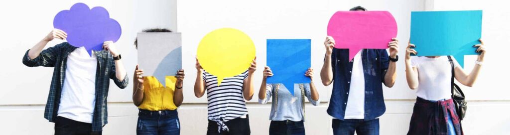 6 people standing in a line against a white background. Their faces are hidden by colourful speech bubble shapes that they are holding up.